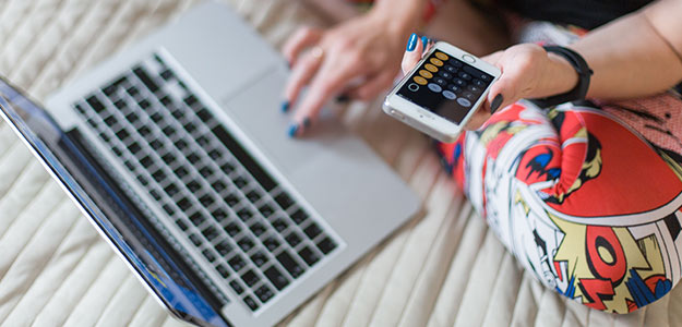 inline image for How America Saves for College 2018. young person with painted nails uses laptop and calculator mobile phone on their bed.