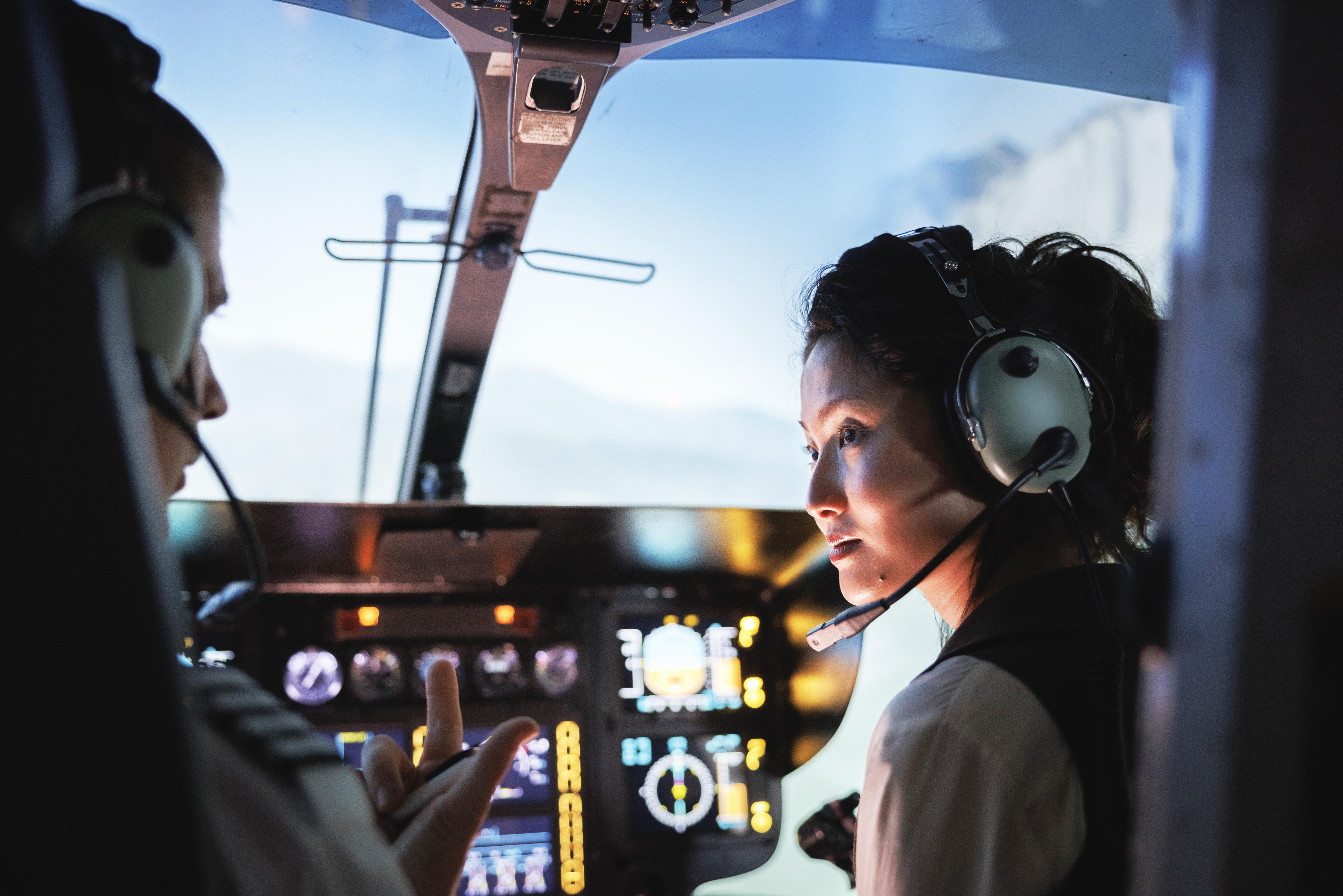 Pilot in discussion with copilot in cockpit in evening.