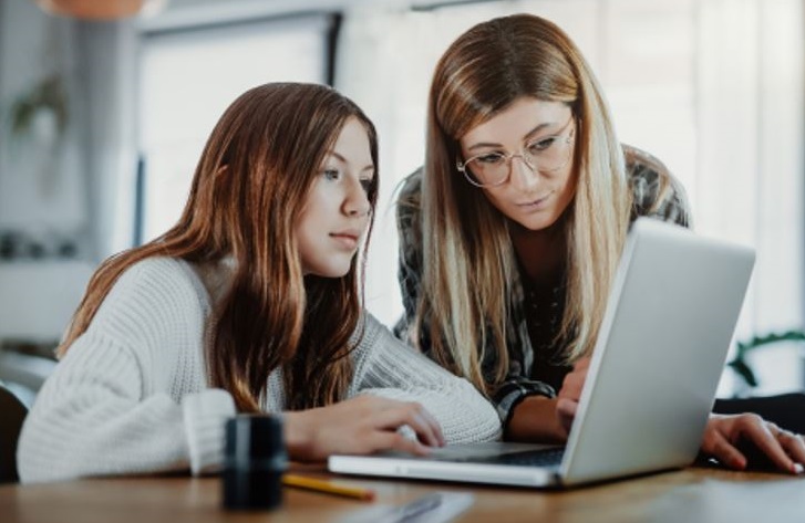 Parent and child looking at a laptop at a table.