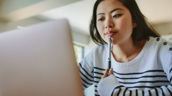 Student sitting in front of a laptop with a pen in their hand.