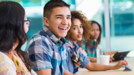 Young male student smiling while sitting with other students.