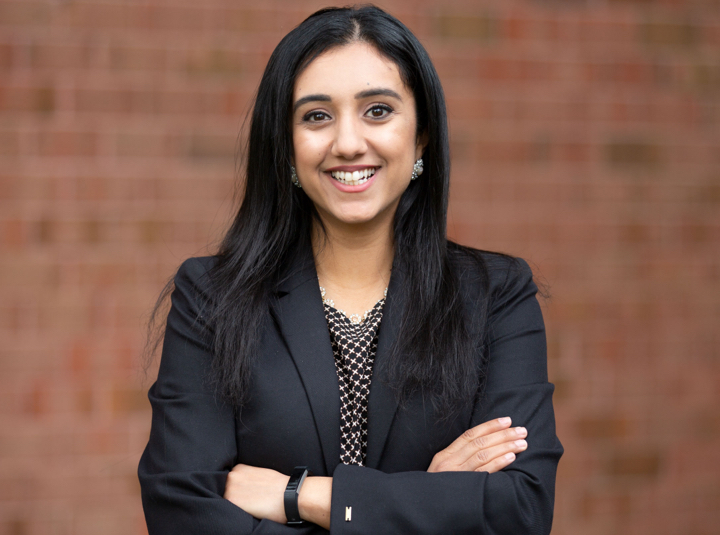 A portrait of Noor H., graduate scholarship winner, smiling straight on to the camera in a black suit.