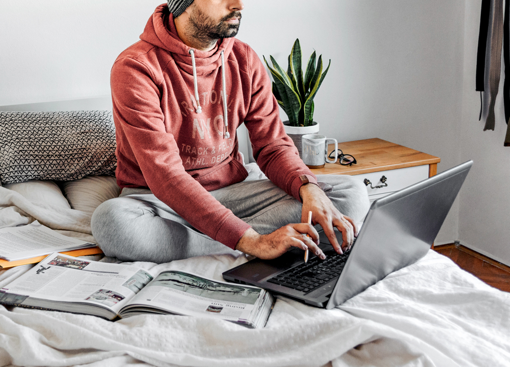 Young man sitting on his bed and typing on his laptop