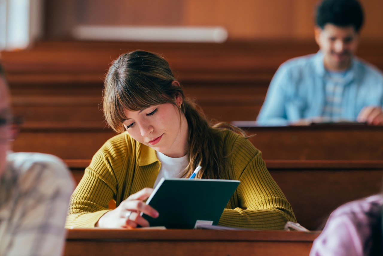 Student in lecture hall taking notes.