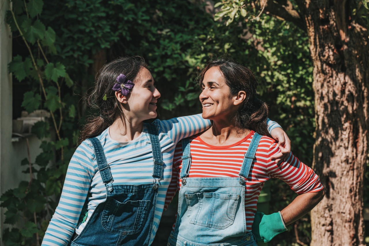 Mother and daughter outside gardening, looking at each other and side-hugging.