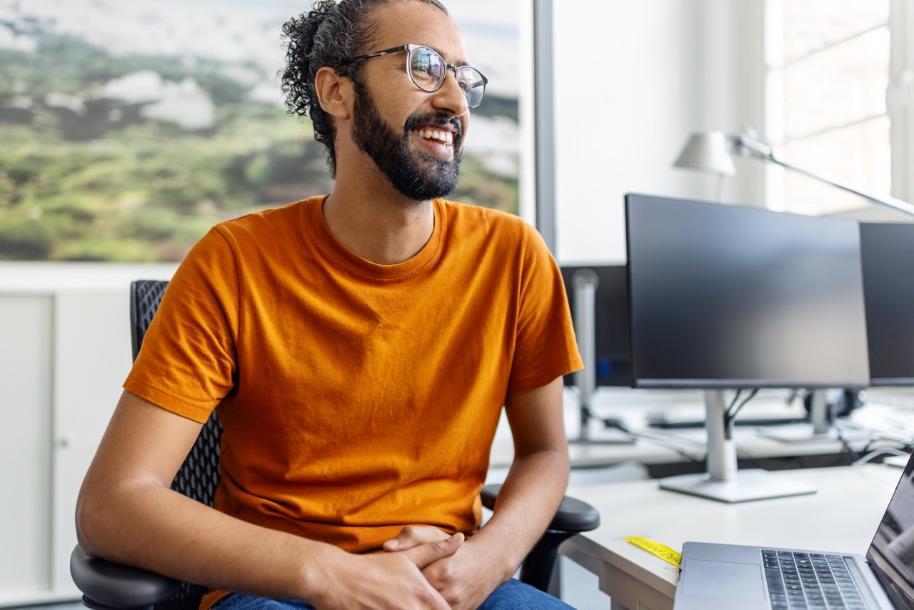 Casual and relaxed graduate student smiling at office desk.